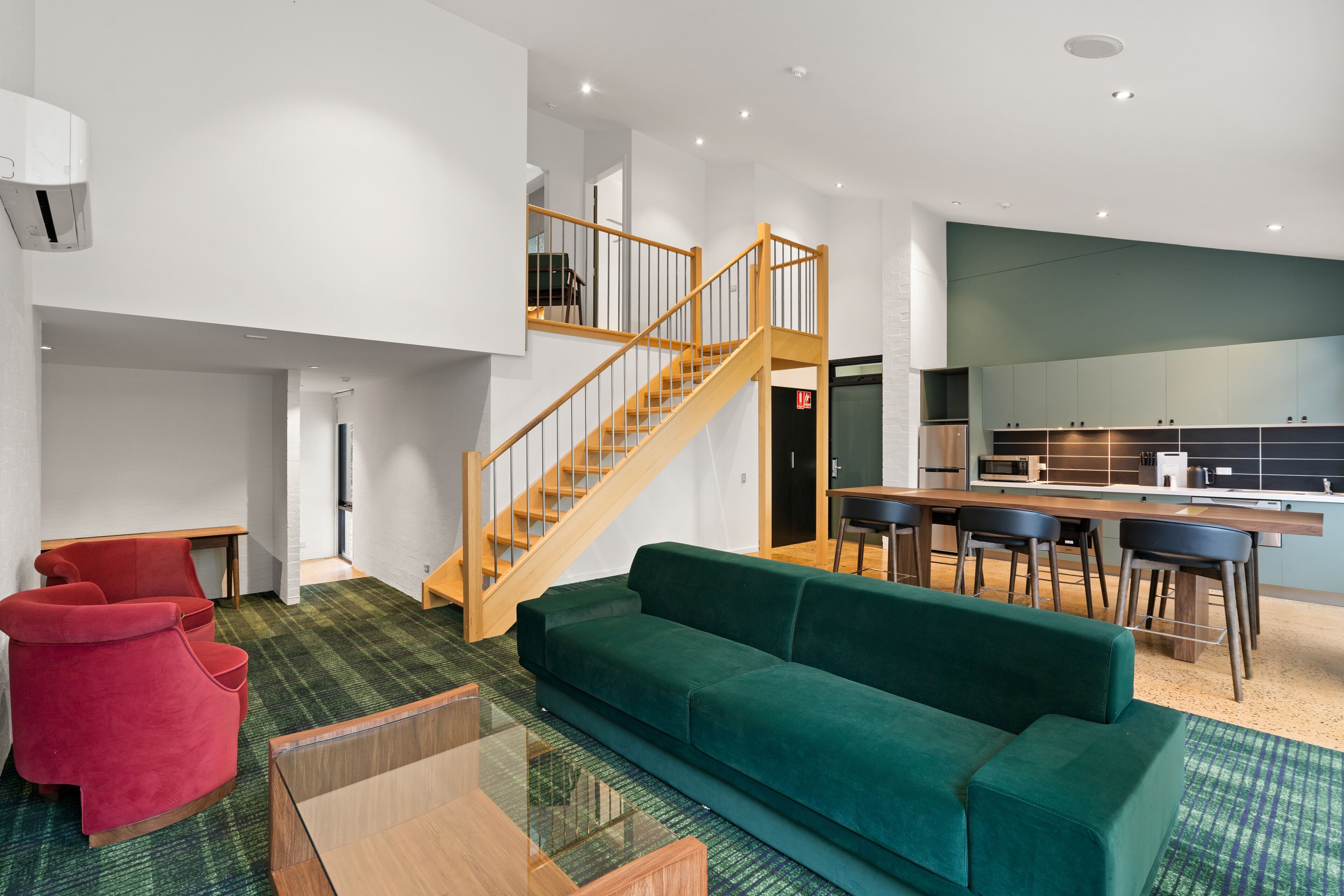 Ein modernes Wohnzimmer mit einem grünen Sofa, einem roten Sessel und einer Holztreppe, die in eine obere Ebene führt.
