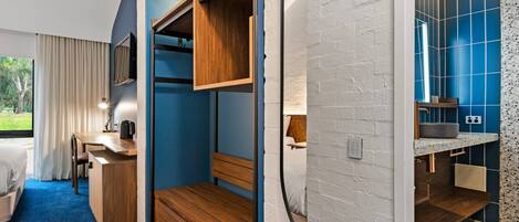 A modern hotel room with a wooden desk, a bed, and a bathroom with blue tiles.