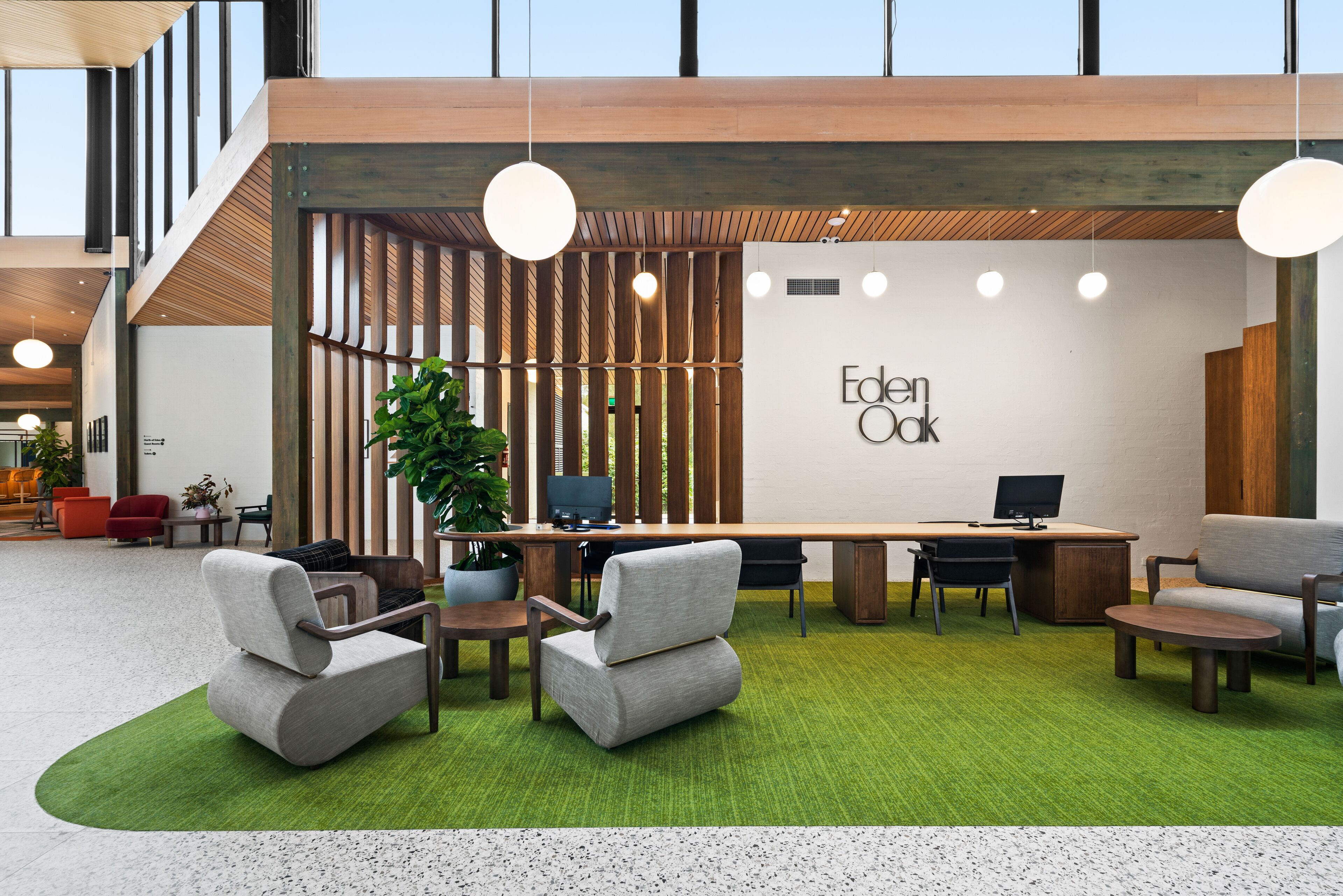 Un espacio de oficina moderno con alfombra verde, escritorios de madera y asientos cómodos.