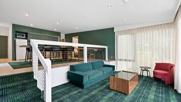 A modern living room with a green sofa, a red chair, and a glass coffee table.
