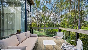 Una terraza moderna al aire libre con un sofá, sillas y una mesa, con vistas a un jardín exuberante y árboles.