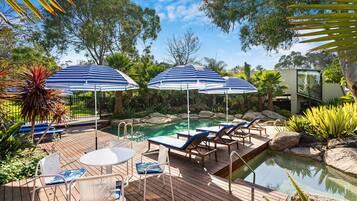 A wooden deck with a pool, lounge chairs, and striped umbrellas.