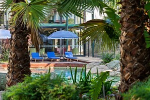 A pool area with lounge chairs and umbrellas, surrounded by palm trees and greenery. - Eden Oak Geelong (East Geelong)