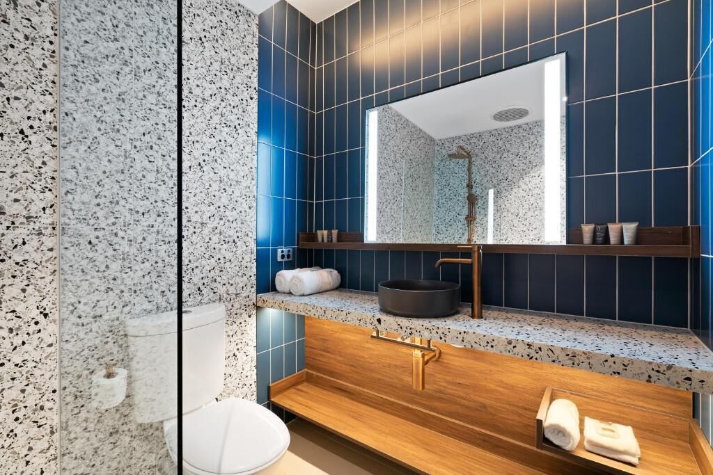 Un baño moderno con encimera de granito, tocador de madera, un espejo grande y zona de ducha.