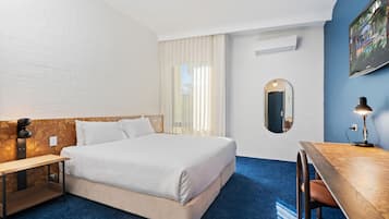 Habitación de hotel con cama, mesita de noche, escritorio, silla y televisión en la pared.
