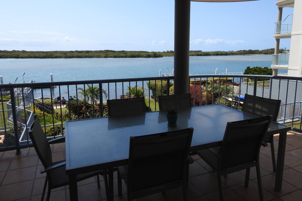 A terrace with a table and chairs, overlooking a body of water and greenery.