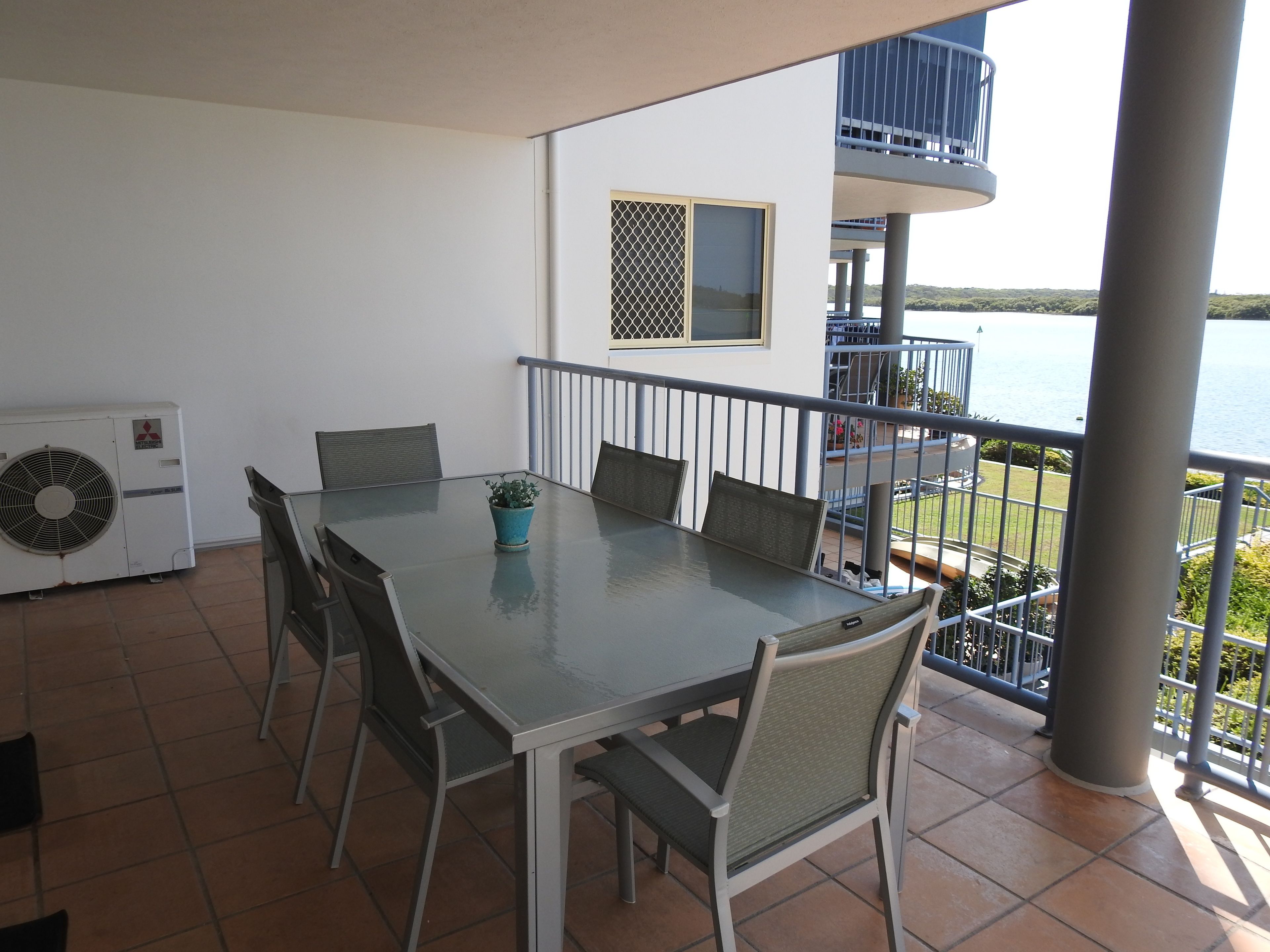 Une terrasse avec une table et des chaises, un pot de fleurs et un appareil de climatisation.