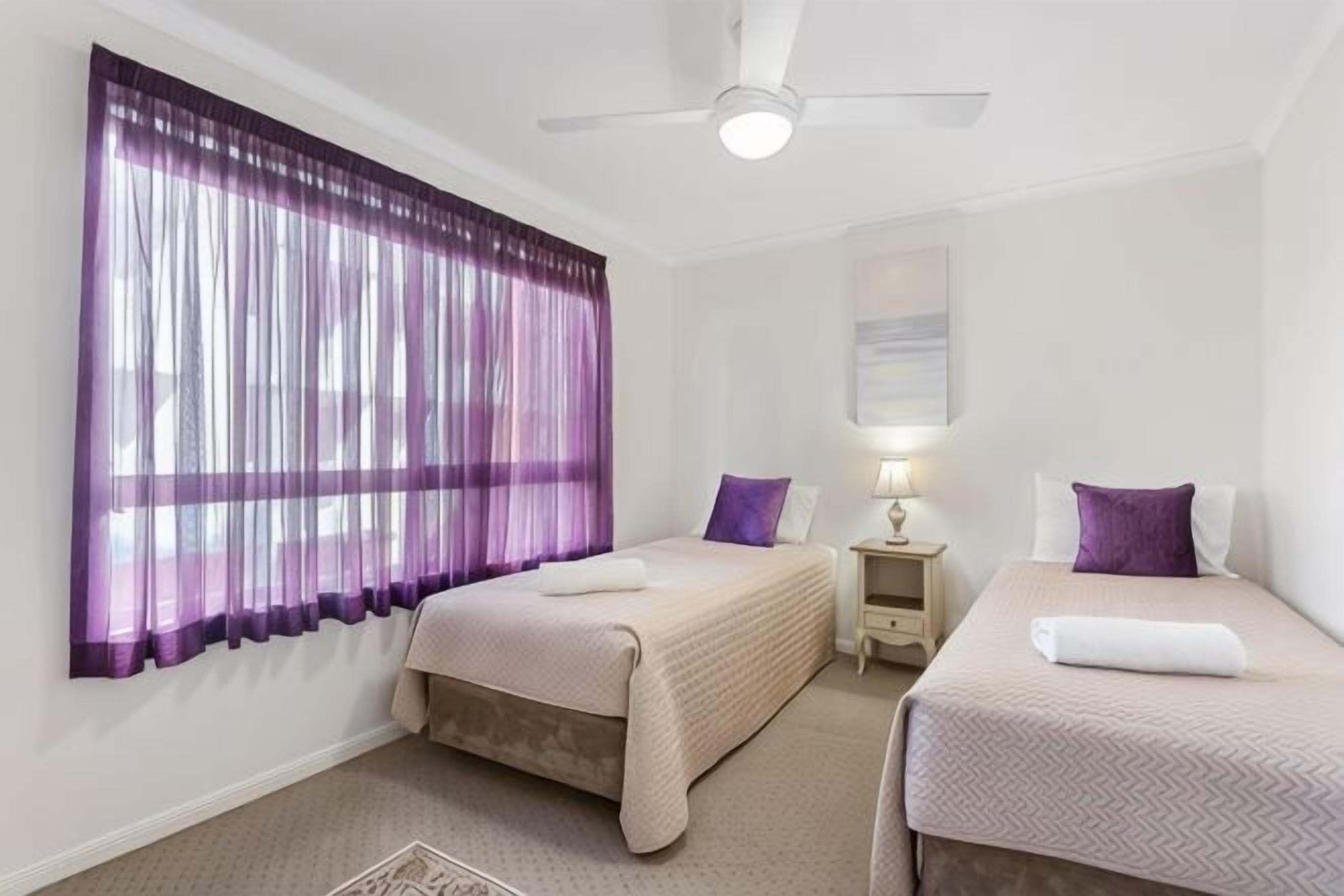 A hotel room with two beds, a ceiling fan, a nightstand, and a lamp.