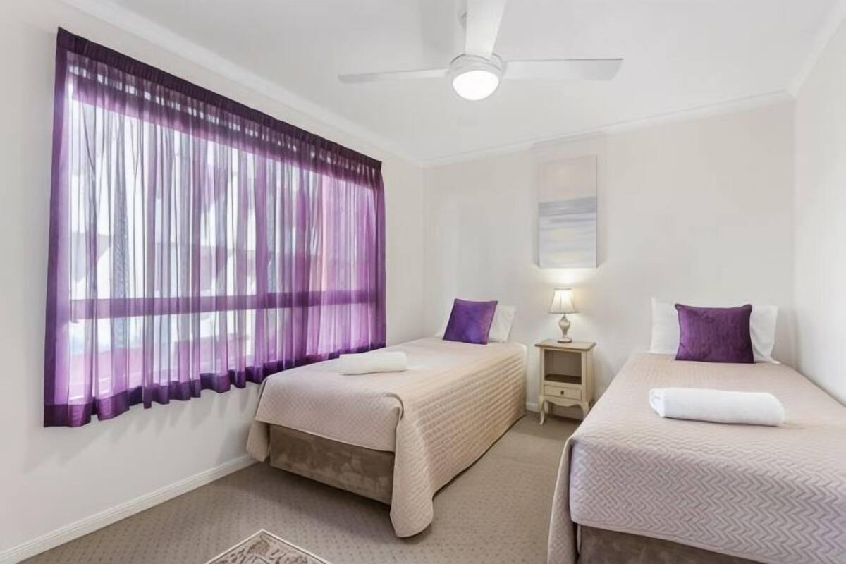 A hotel room with two beds, a ceiling fan, a nightstand, and a lamp.