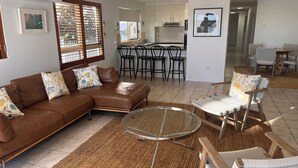 A spacious living room with a brown leather sofa, a glass coffee table, and a dining area with chairs and a table. - On The River Apartments (Maroochydore)