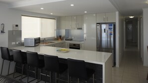A modern kitchen with a central island, bar stools, a refrigerator, and a microwave. - On The River Apartments (Maroochydore)