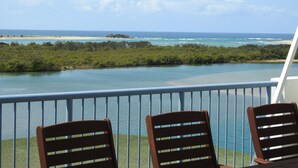 A balcony with two wooden chairs facing a view of the ocean and a beach. - On The River Apartments (Maroochydore)