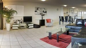 A modern living room with a black leather sofa, a glass coffee table, and a red rug. - On The River Apartments (Maroochydore)