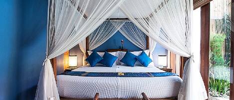 A bedroom with a canopy bed, wooden headboard, and a view of greenery outside.