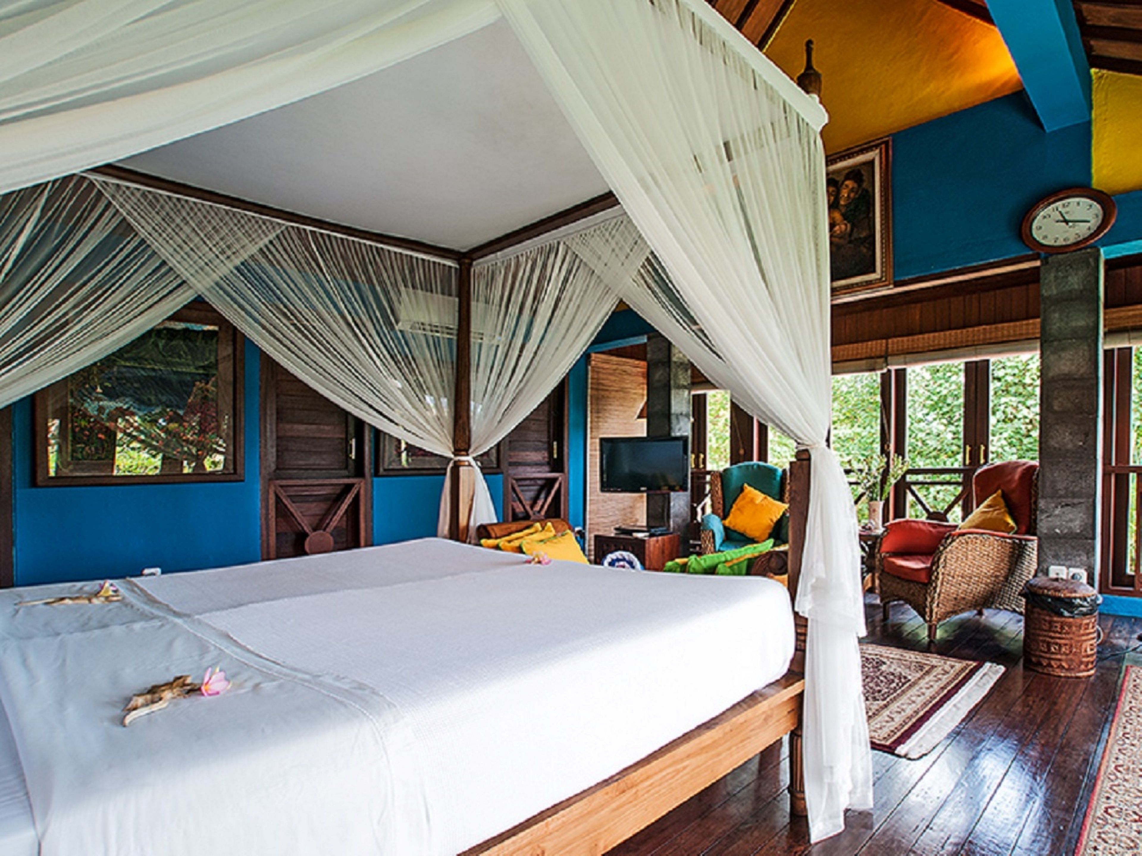 A room with a bed, a television, and a seating area with chairs and cushions.