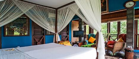 A room with a bed, a television, and a seating area with chairs and cushions.