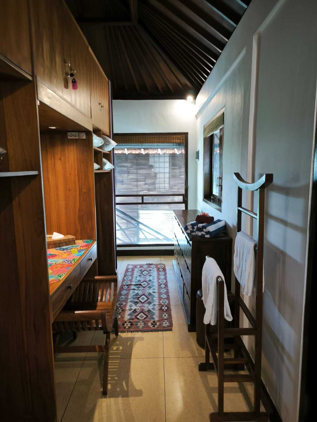 Ein kleines Zimmer mit einem Holzschrank, einem Schreibtisch, einem Stuhl und einem Fenster mit Jalousien.