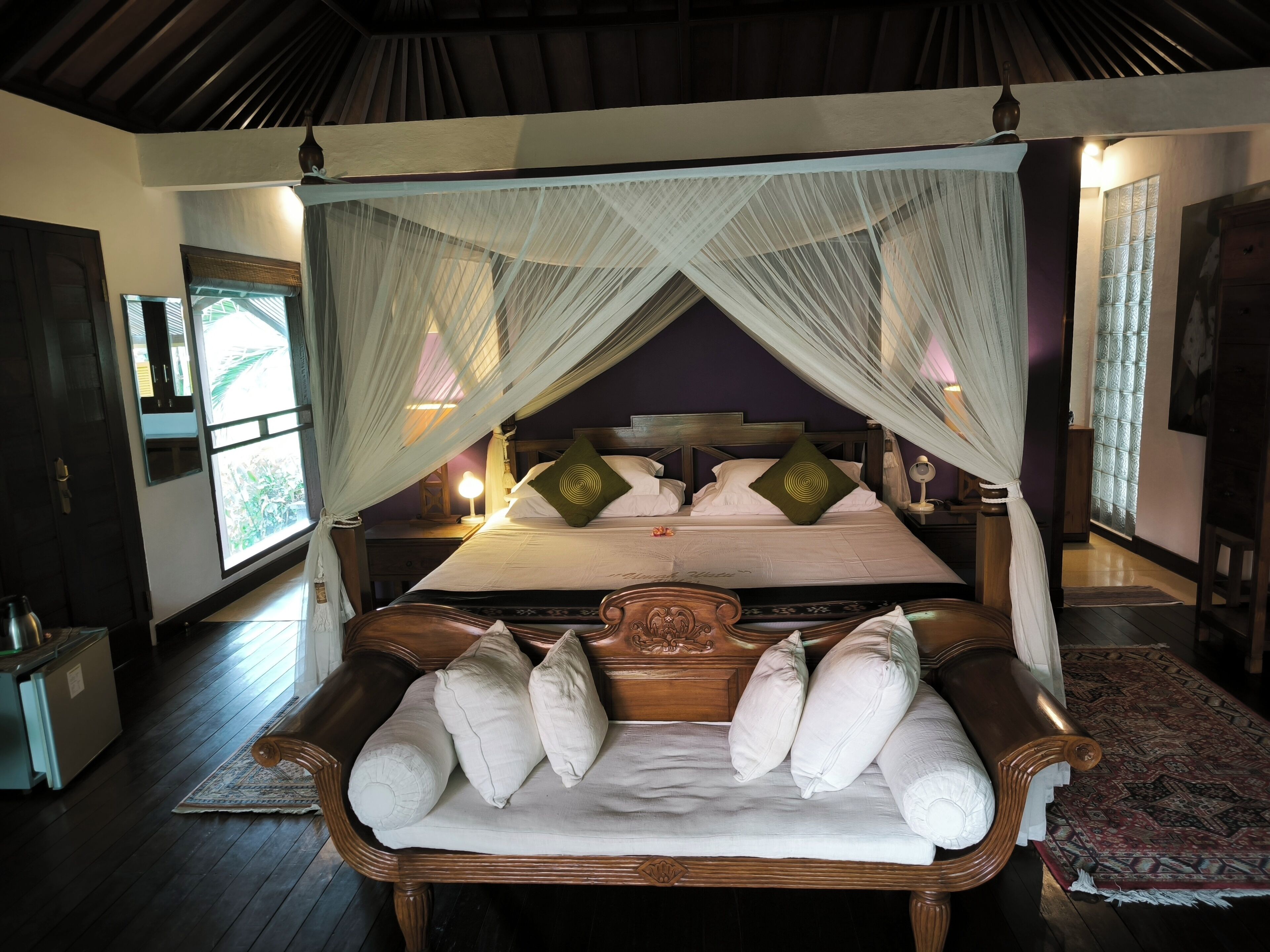 A bedroom with a four-poster bed, a wooden bench with cushions, and a canopy.