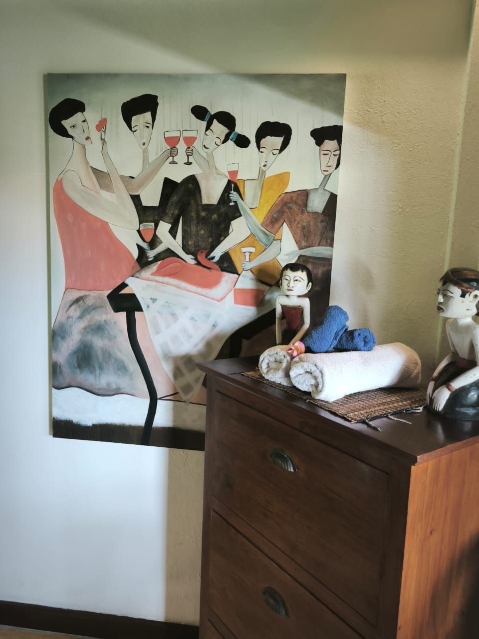 Ein Gemälde, das eine Gruppe von Personen auf einem Bett, eine Kommode mit einem aufgerollten Handtuch und eine kleine Figur zeigt.