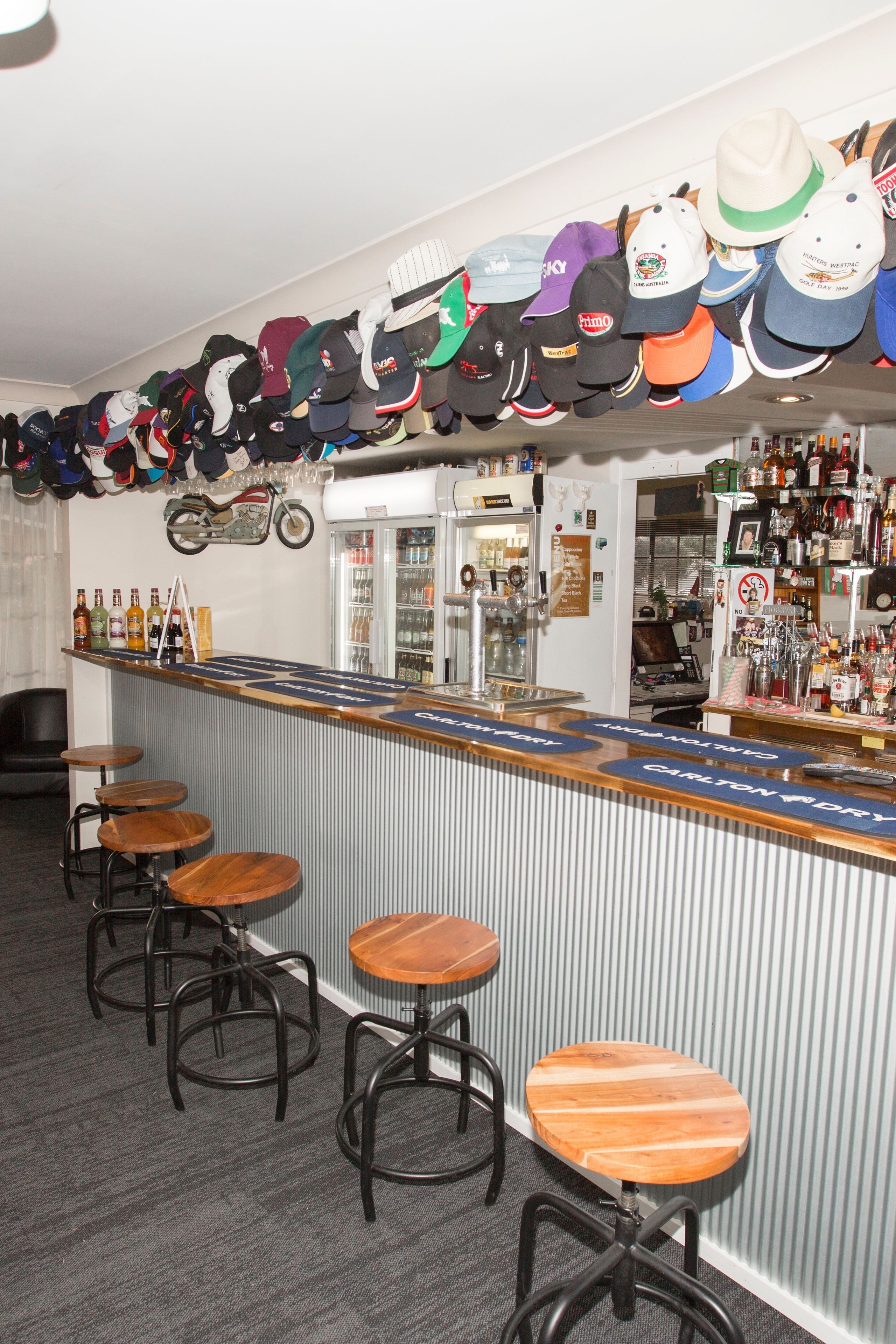 Un espace bar avec un comptoir, des tabourets et un mur où sont exposés différents chapeaux.