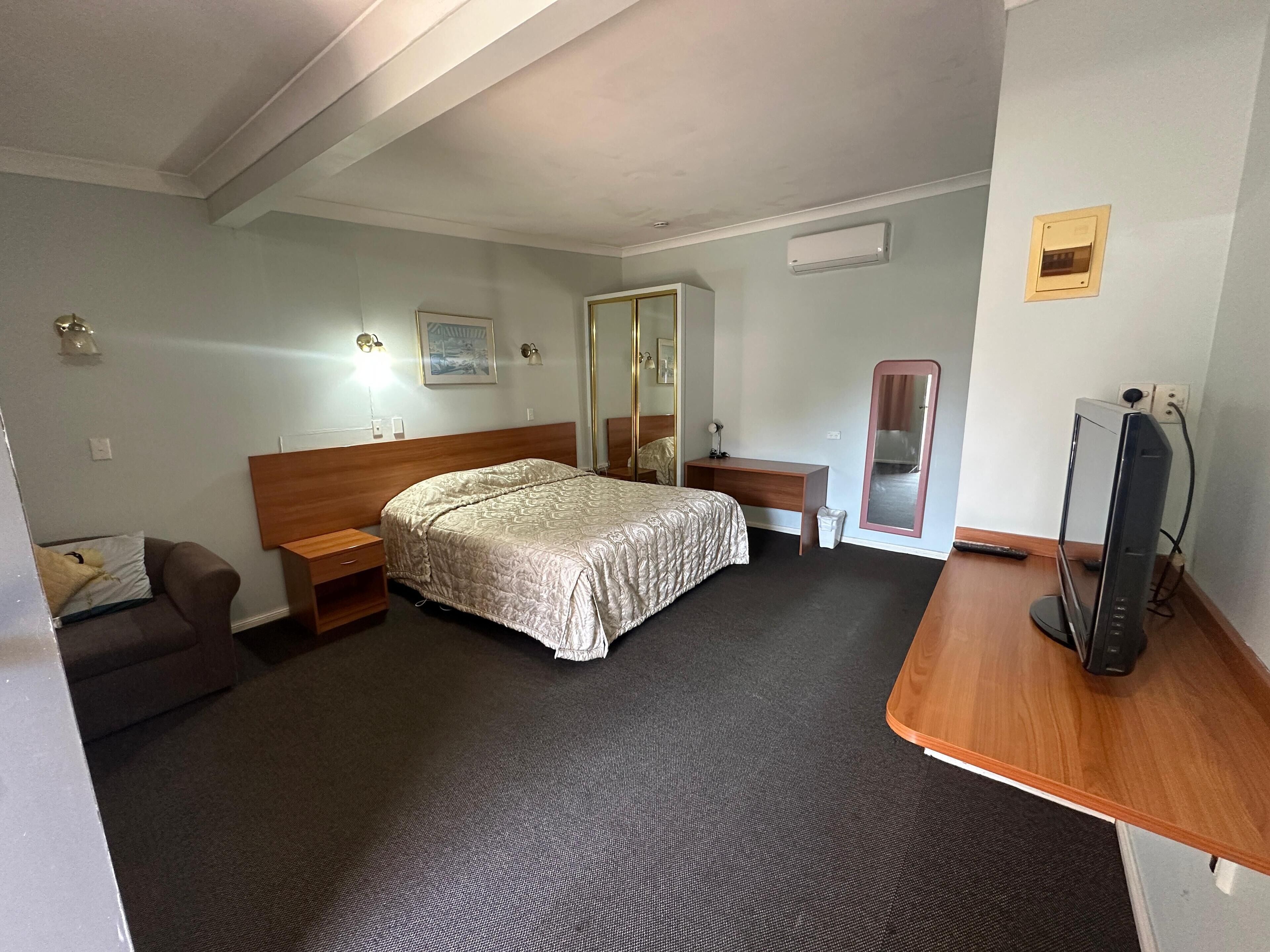 Una habitación de hotel con cama, escritorio, silla, televisor y espejo.