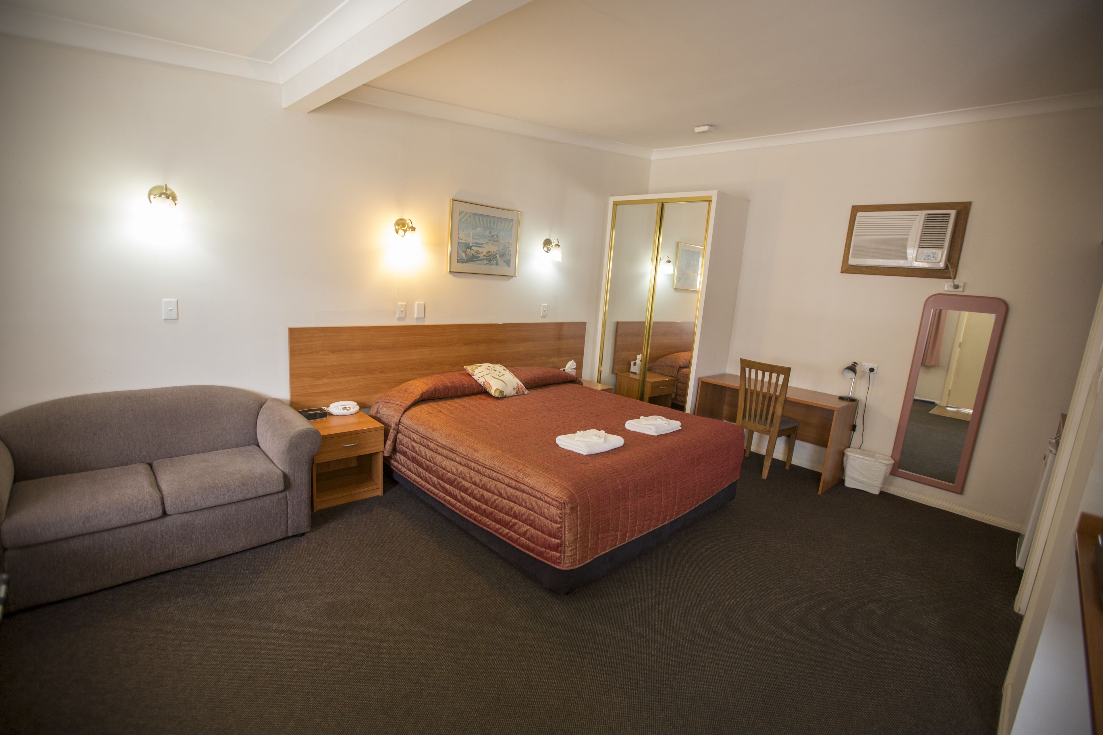 A hotel room with a bed, a sofa, a desk, and a mirror.