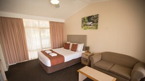 A hotel room with a bed, a bedside table, a sofa, and a painting on the wall. - Colonial Motor Lodge Scone (Scone)