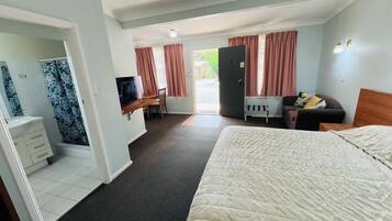 A hotel room with a bed, a desk with a TV, a wardrobe, and a view of the outside.