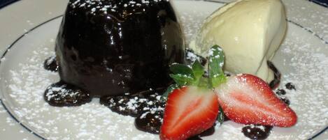 Un plato de postre con un pastel volcán de chocolate, una bola de helado de vainilla y una fresa.