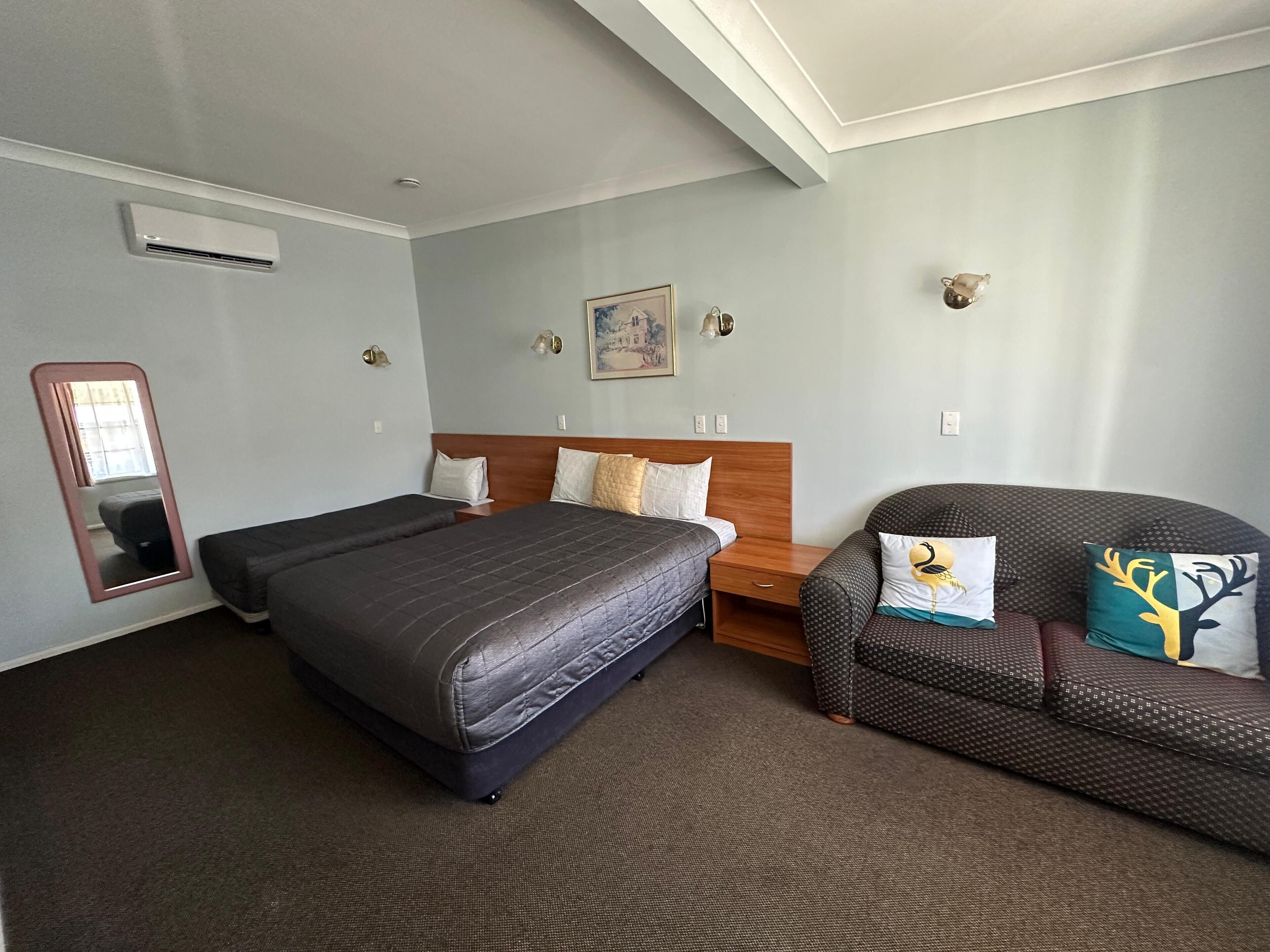 Quarto de hotel com uma cama grande, uma cadeira, uma mesa de cabeceira, um espelho e um quadro na parede.