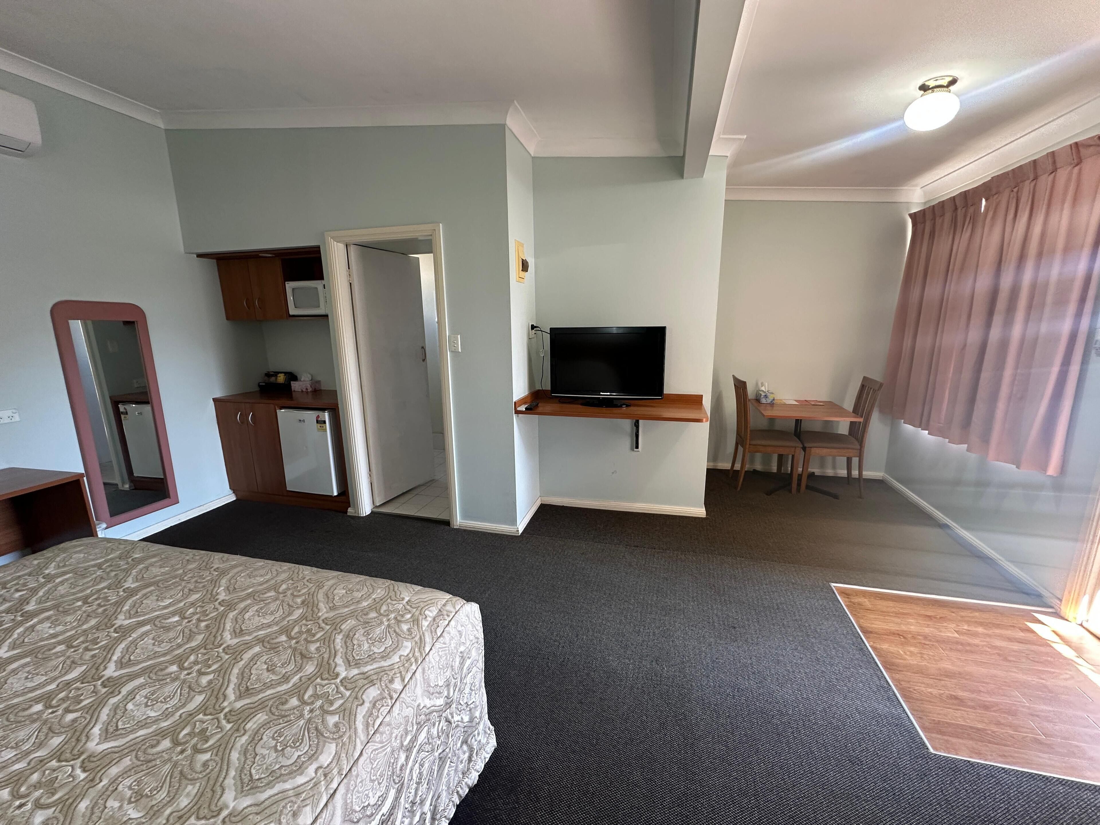 Une chambre d’hôtel comprenant un lit, un bureau avec une télévision, une petite kitchenette et un coin repas.