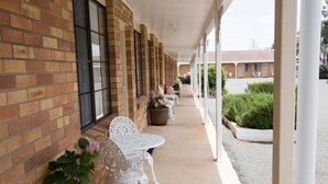 A covered outdoor area with brick walls, white metal chairs, and potted plants. - Colonial Motor Lodge Scone (Scone)