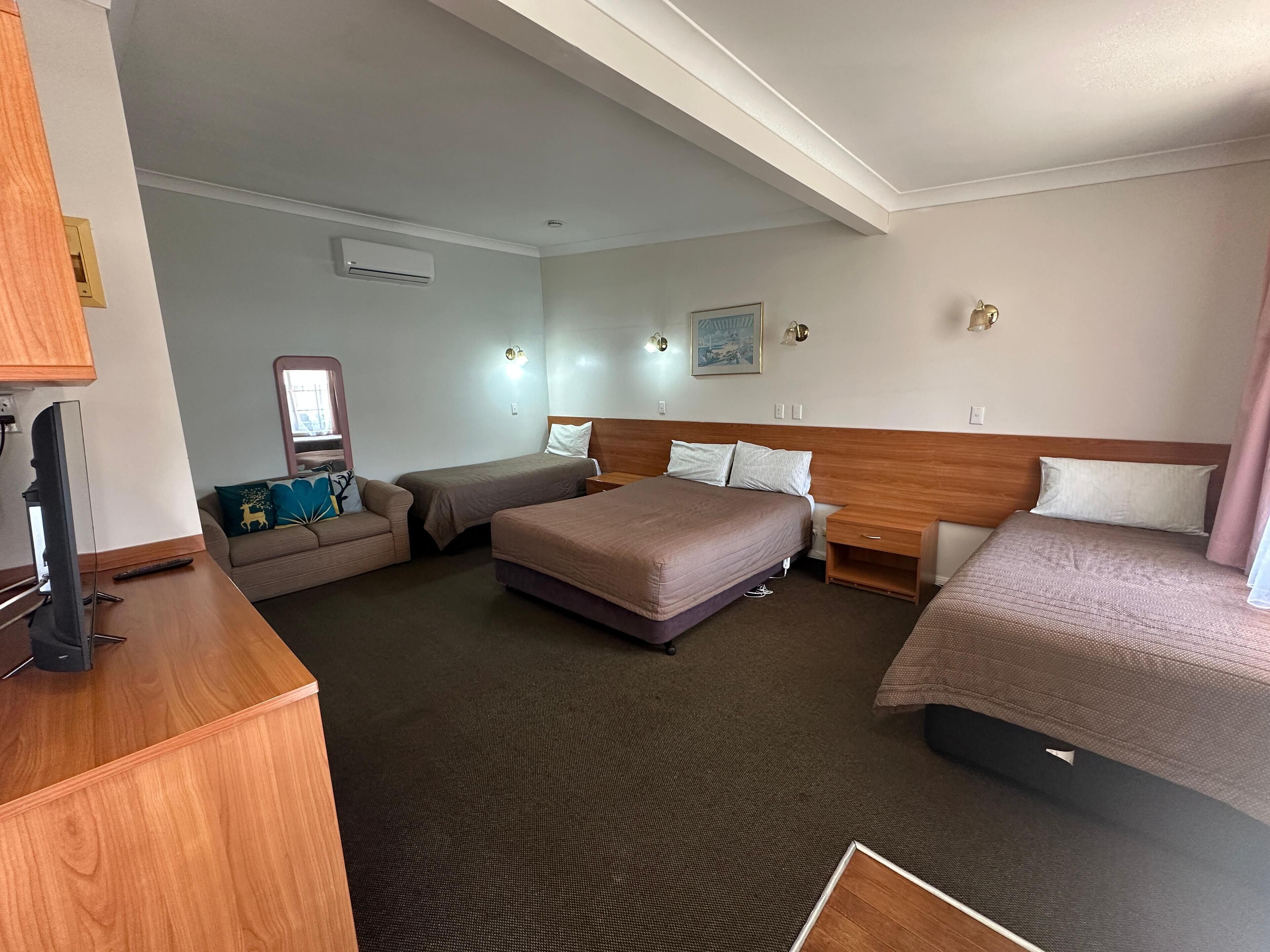 Habitación de hotel con dos camas individuales, un sofá, un televisor y un escritorio de madera.