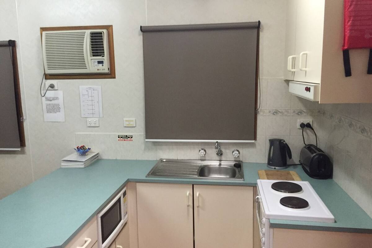 Cocina compacta con lavamanos, estufa, microondas y ventana con persiana.