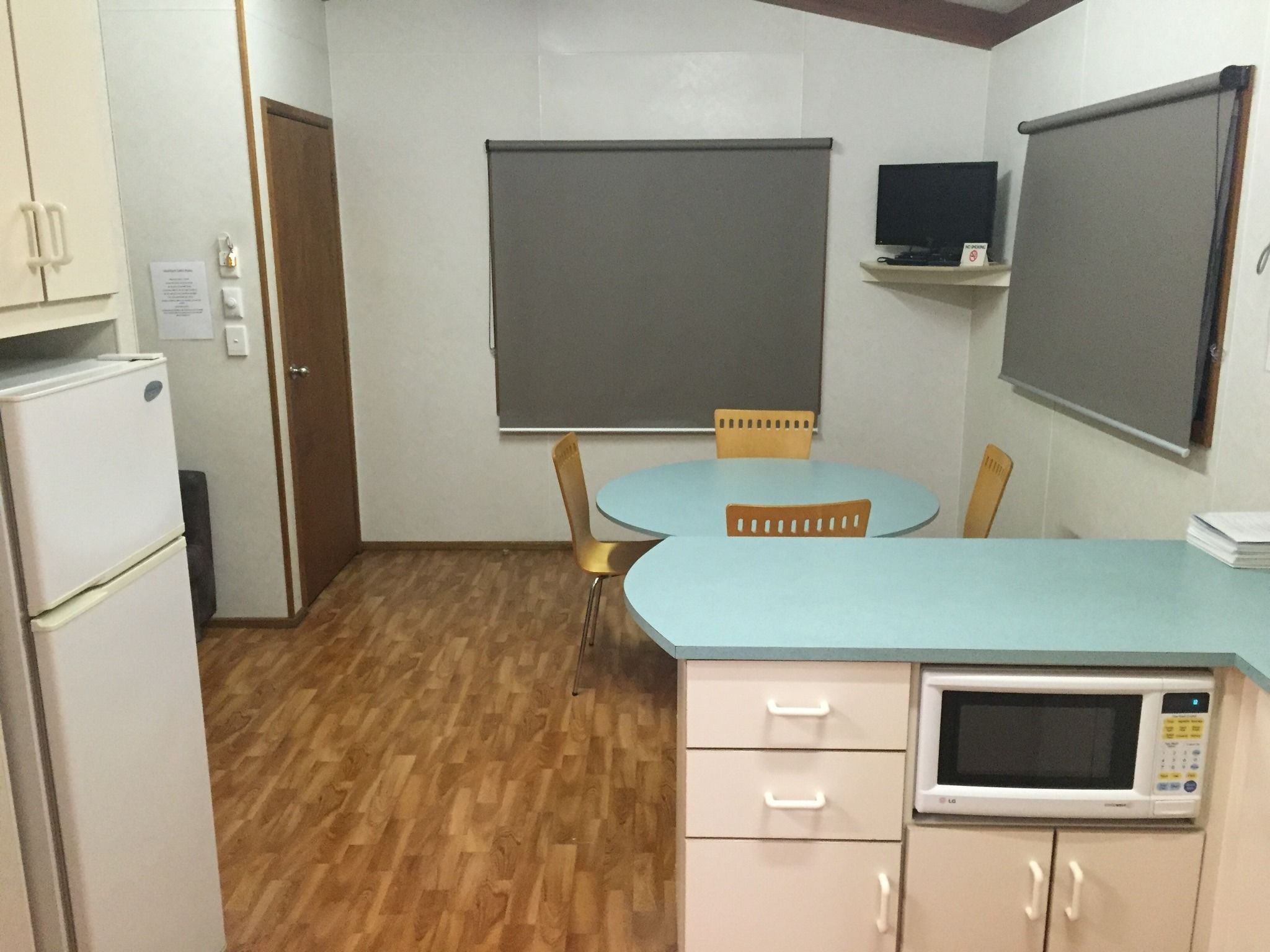 Una cocina compacta con microondas, refrigerador, lavamanos y una mesa con sillas.