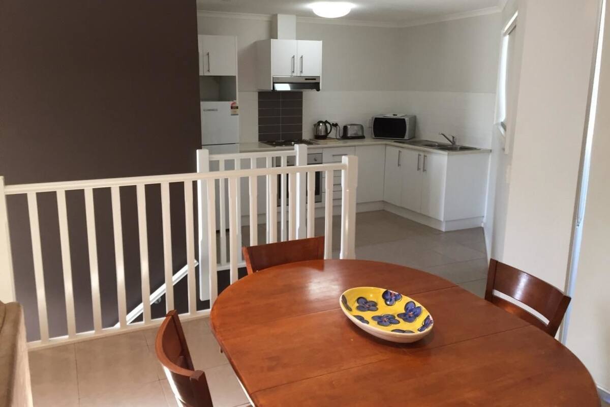 Un comedor con una mesa y sillas de madera, un cuenco con diseño floral y una cocina al fondo.