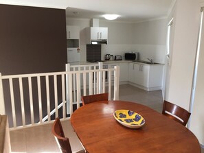 A dining area with a wooden table and chairs, a bowl with a floral pattern, and a kitchen in the background. - Inverloch Cabins (Inverloch)