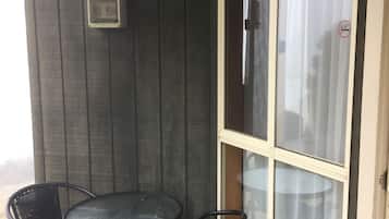 A small patio with a round table and two chairs, a window with a curtain, and a wooden bench.