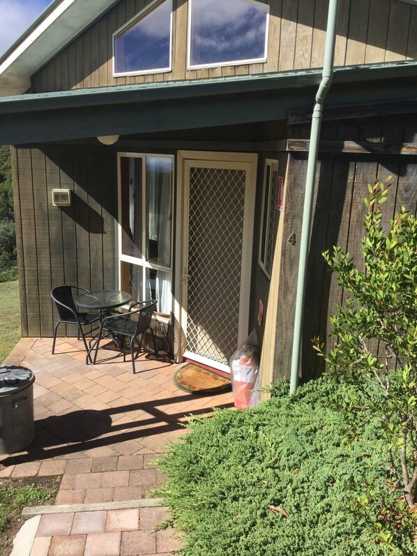 A wooden house with a covered patio, a table and chairs, and a trash can. - Jenolan Cabins (Jenolan)