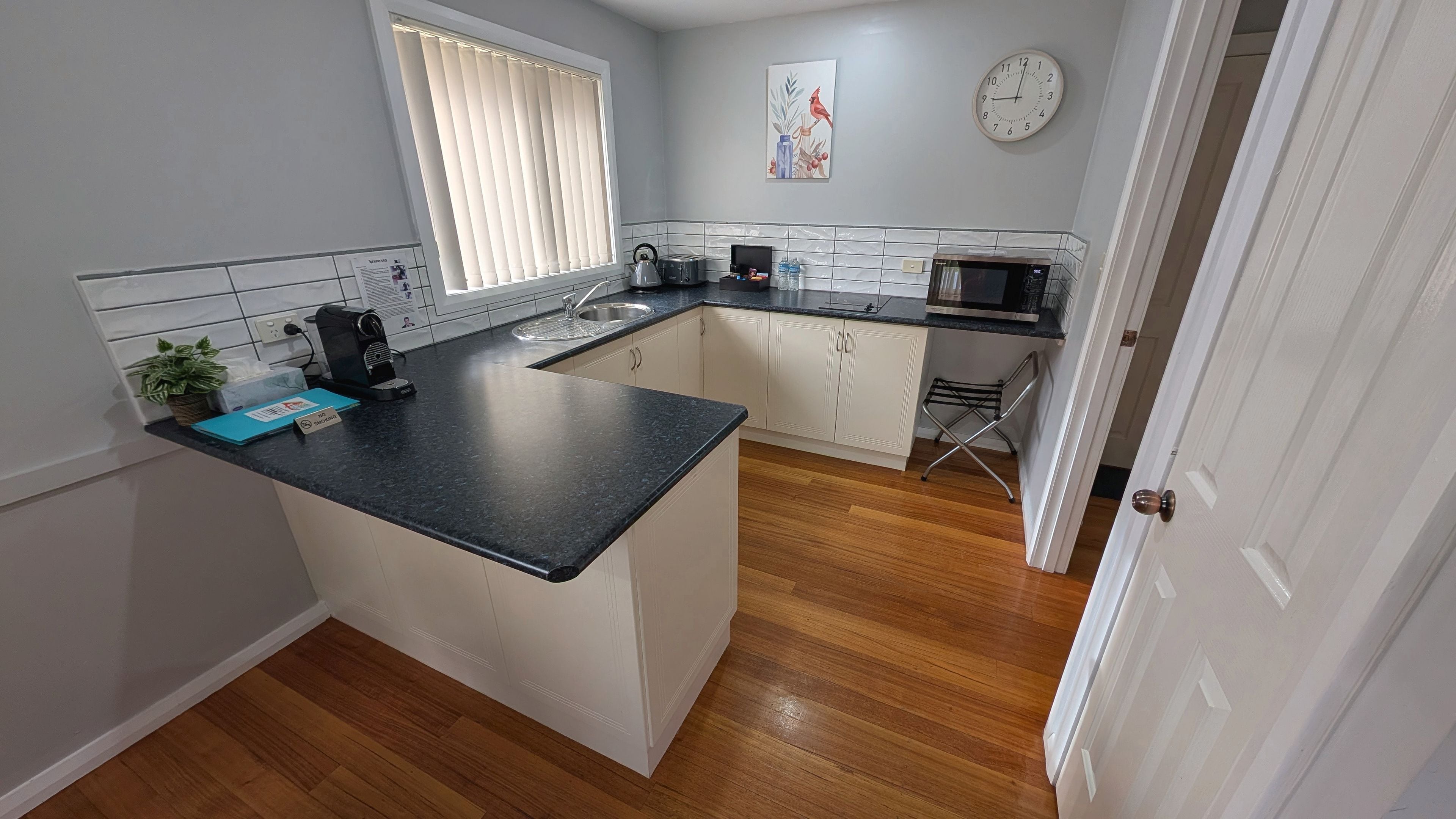 A kitchen with a black countertop, white cabinets, a microwave, a kettle, and a sink.