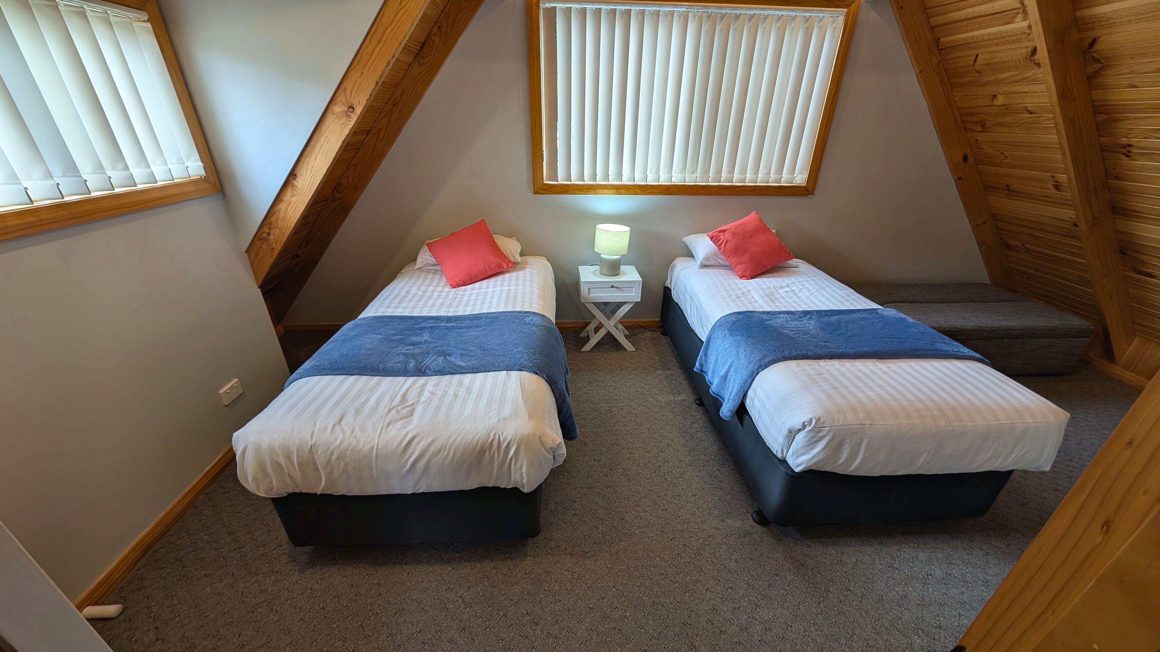 A bedroom with two beds, a nightstand with a lamp, and a window with blinds.