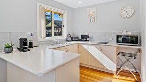 A modern kitchen with a large island, a built-in oven, and a window with a view of a house and trees. - Four Seasons Waterfront Villas (Taranna)