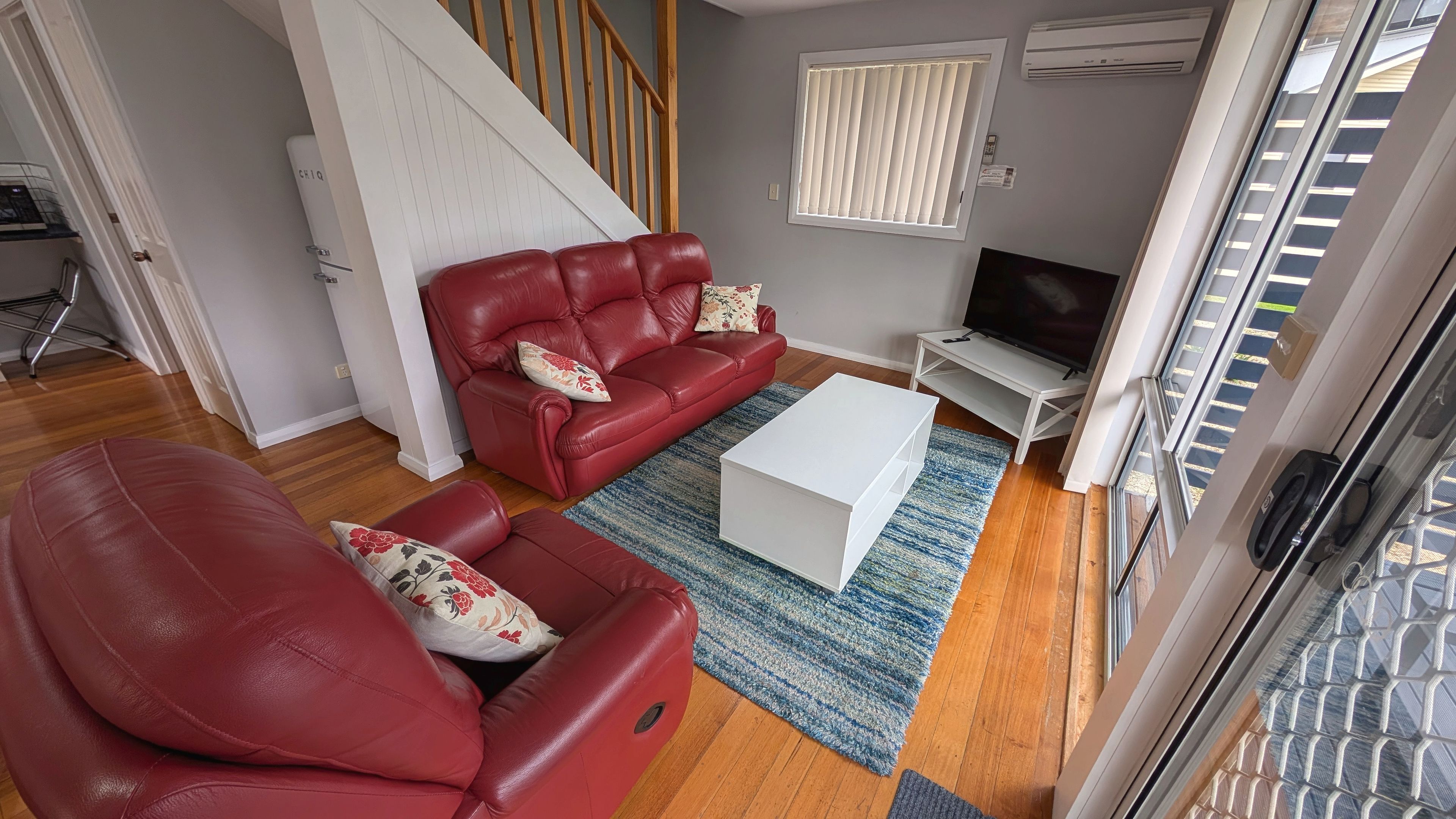 A living room with a red leather sofa, a white coffee table, and a TV on a stand.