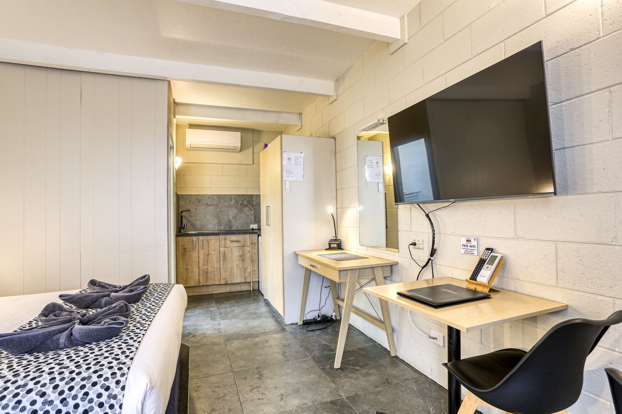 Ein kleines Hotelzimmer mit Bett, Schreibtisch, Stuhl, Fernseher und einer kleinen Küchenzeile.