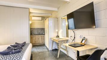Ein kleines Hotelzimmer mit Bett, Schreibtisch, Stuhl, Fernseher und einer kleinen Küchenzeile.