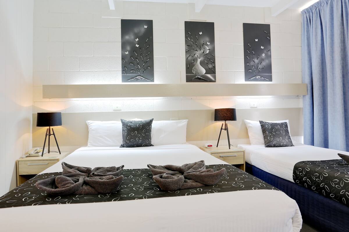 A hotel room with two beds, a large wall art piece above the beds, and a blue curtain on the right.