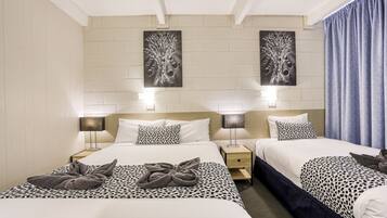 A hotel room with two beds, each with a patterned bedspread and a towel on the bed. There are wall-mounted lamps on either side of the beds, and two wall art pieces above the beds.