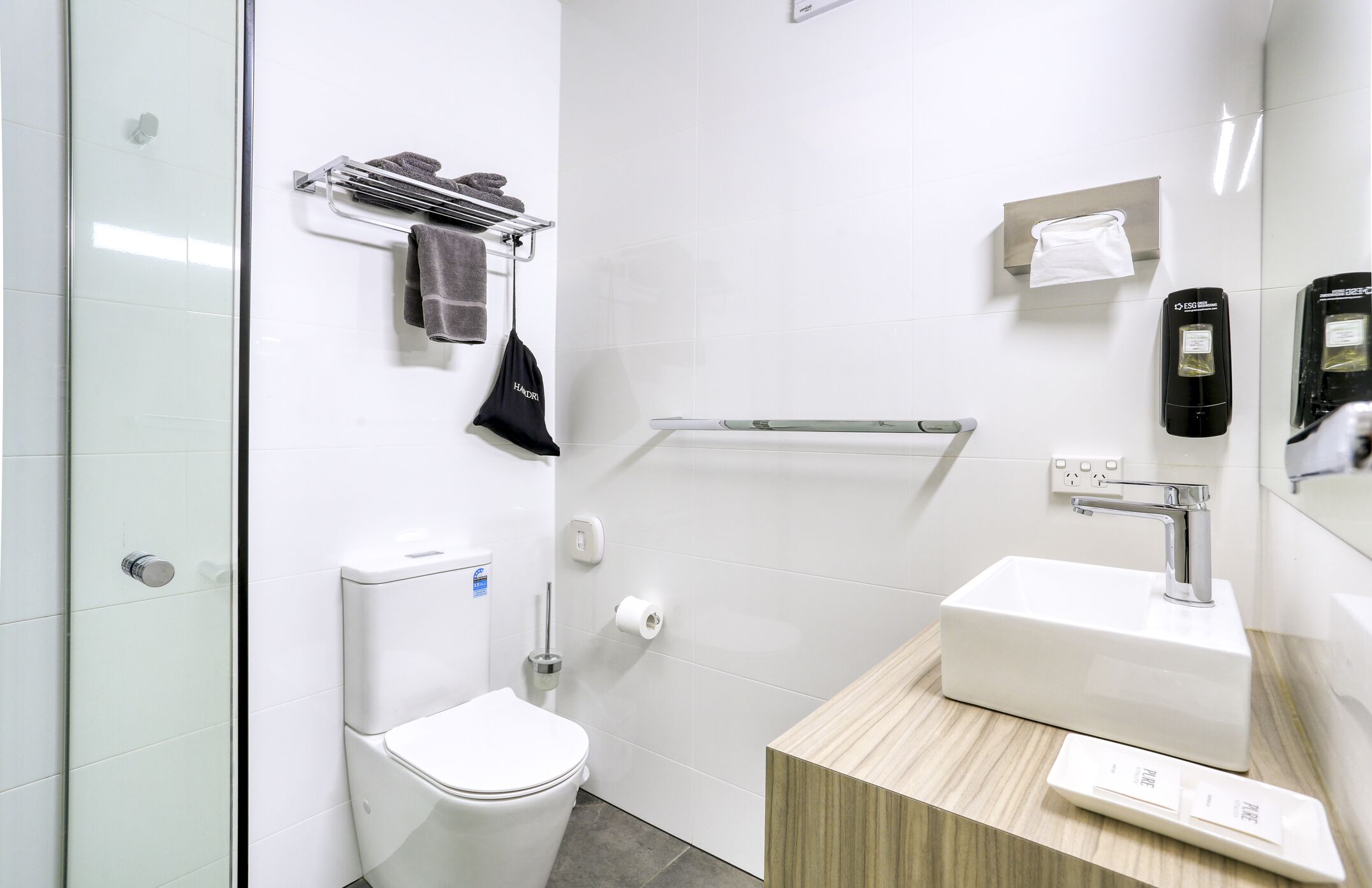 Een moderne badkamer met toilet, wastafel, handdoekrek en handdroger.