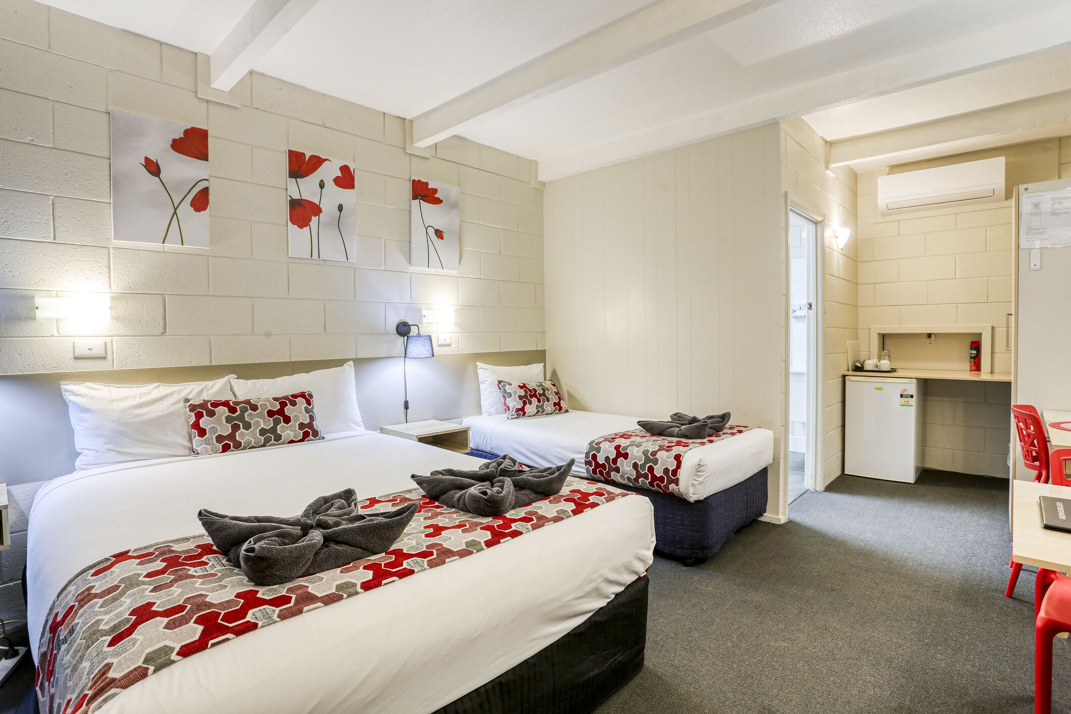 A hotel room with two beds, a small kitchenette, and a desk with a chair.