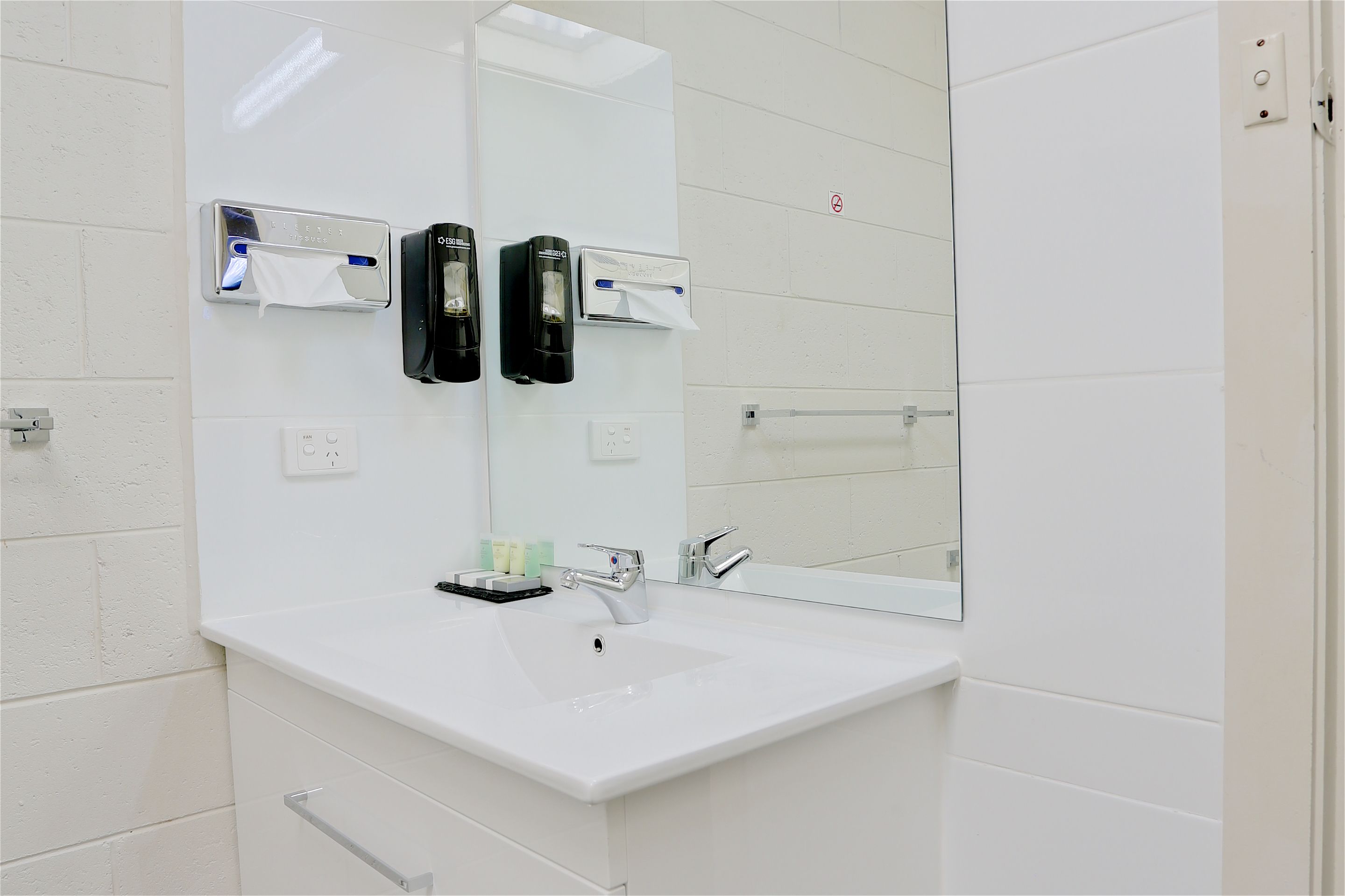 A modern bathroom with a white sink, two paper towel dispensers, and a mirror.